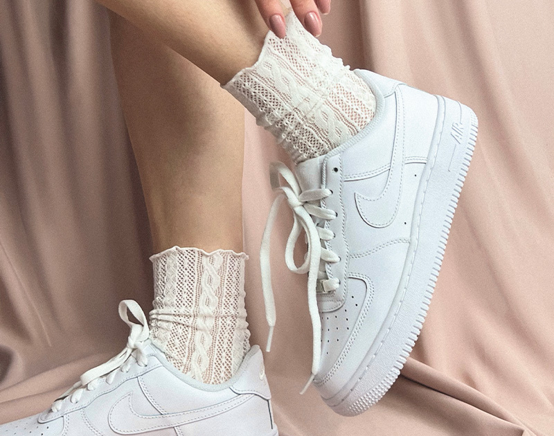 Tênis branco com meia de renda bege, estilo casual e confortável.
