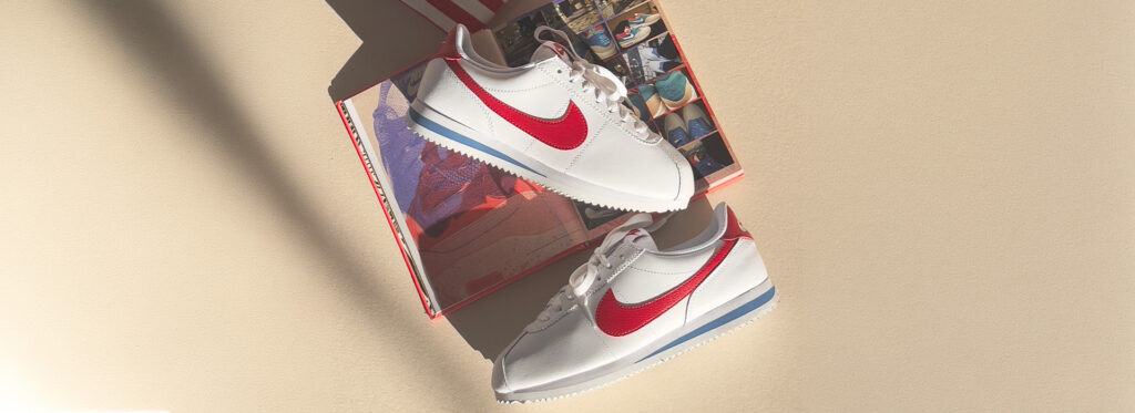 Tênis Nike Cortez branco com detalhes vermelhos e azul em caixa de papelão.