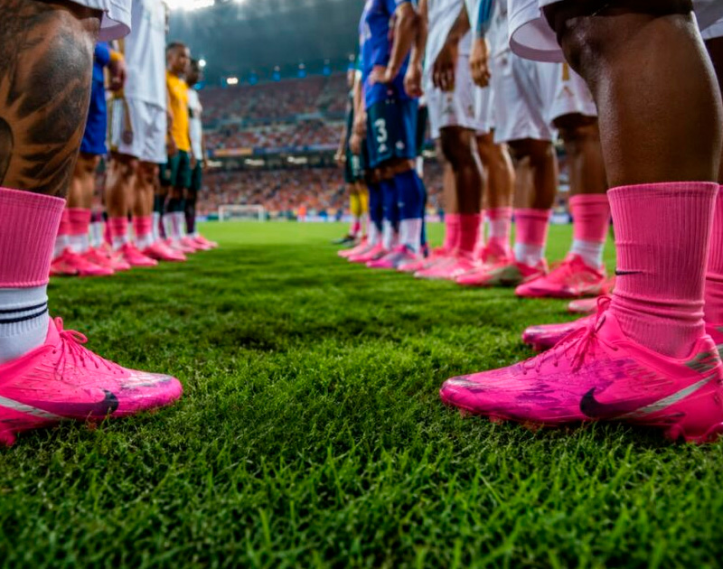 Chuteiras rosa da Nike, Adidas, Puma e New Balance alinhadas no gramado