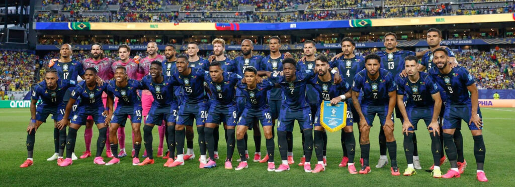 Time de futebol do Brasil posando no estádio com uniformes azuis.