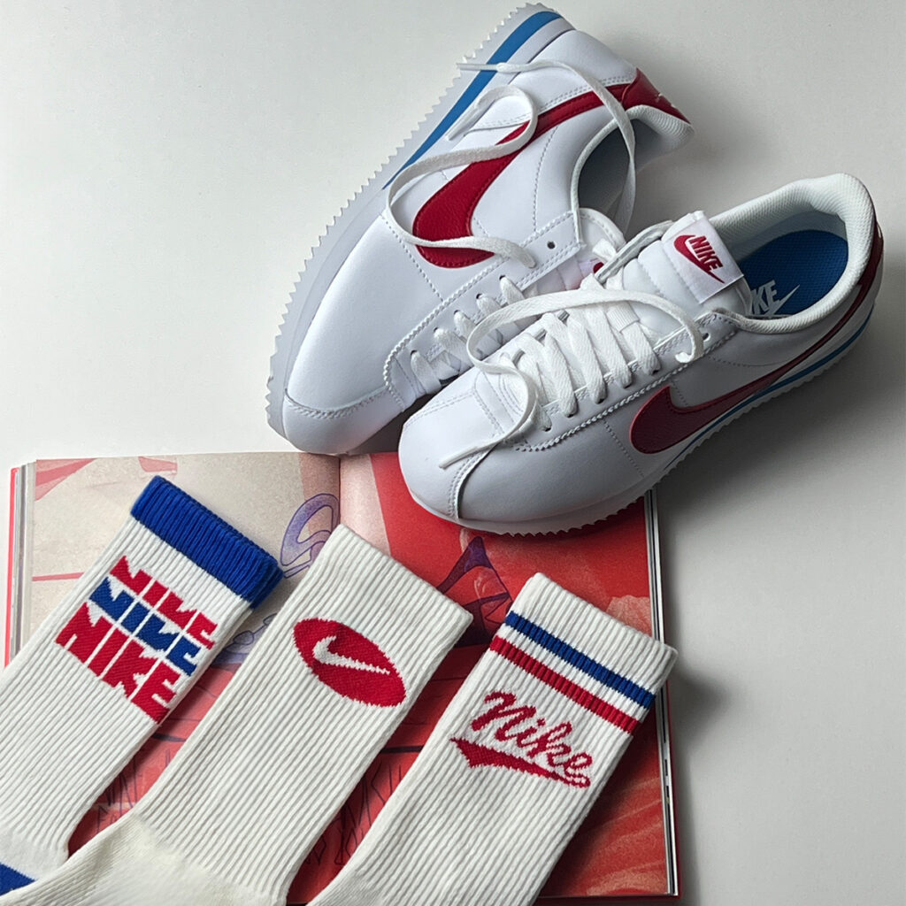 Tênis Nike Cortez branco com detalhes vermelhos e azuis.